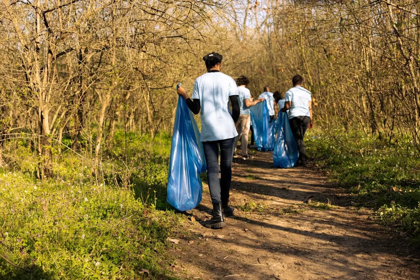 Афроамериканский активист собирает мусор и перерабатываемые отходы в синий пакет.